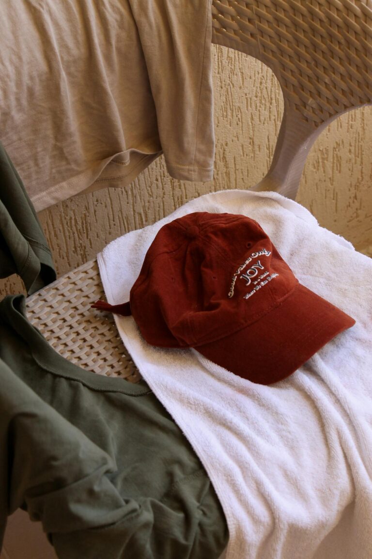 Casual clothes and a red cap laid out on a patio chair with natural light.