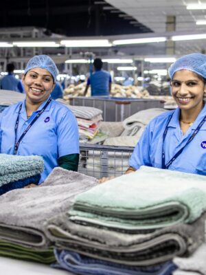 Two female workers in a textile factory sorting folded fabrics with smiles.
