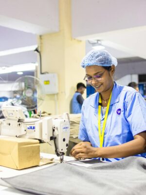 Workers in a textile factory operating sewing machines, wearing blue uniforms and caps.